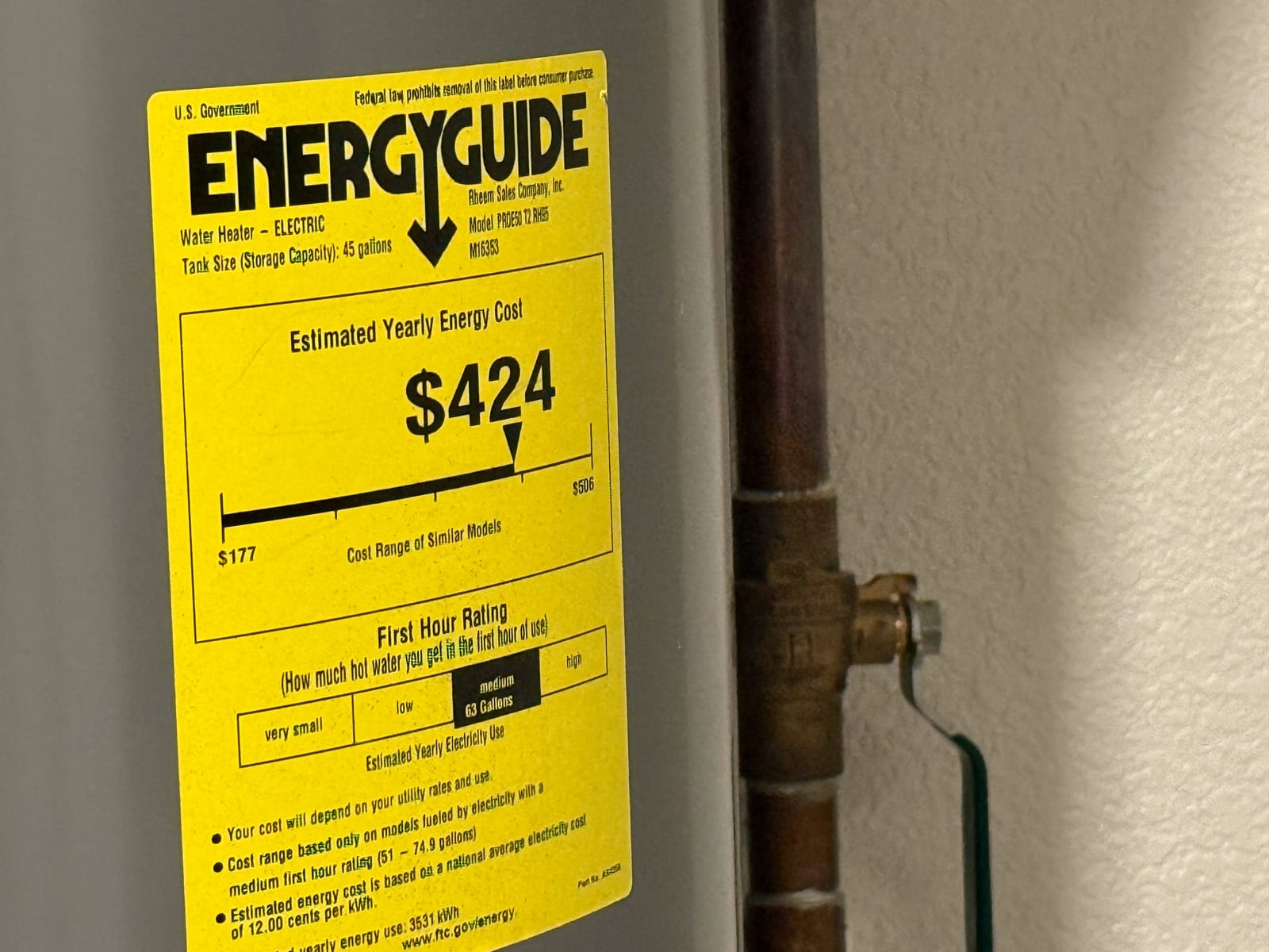 A yellow EnergyGuide label on an electric water heater showing an estimated yearly energy cost of $424 and a first-hour rating of 63 gallons.